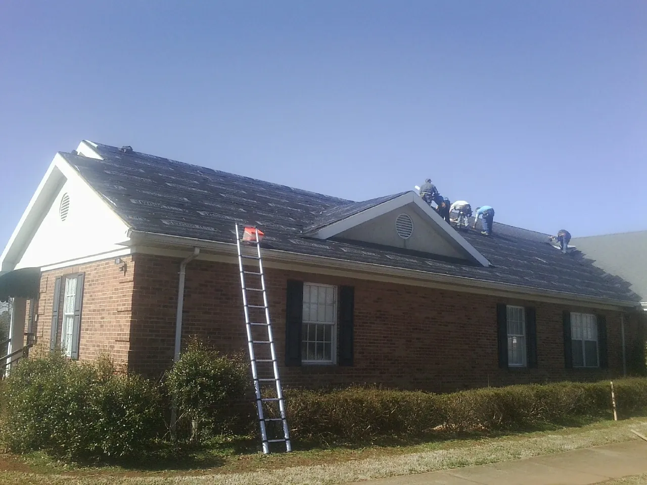 Crew tearing shingles off a brick ranch roof with a ladder set — Emergency Roof Repair work by our crew in Southington
