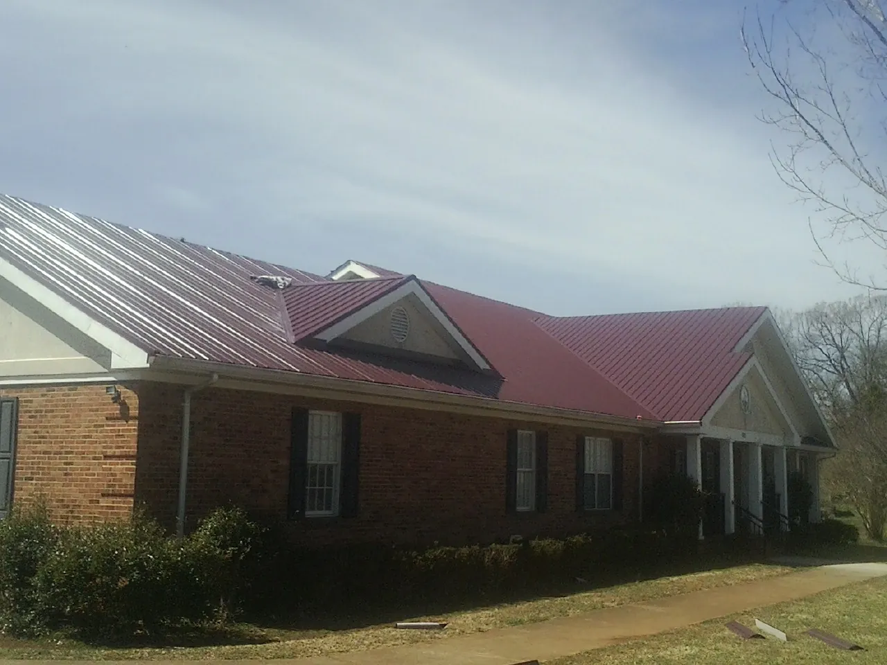 Red metal roof with gabled entries on a long brick building, from a Hail Damage Roof Repair job in Southington