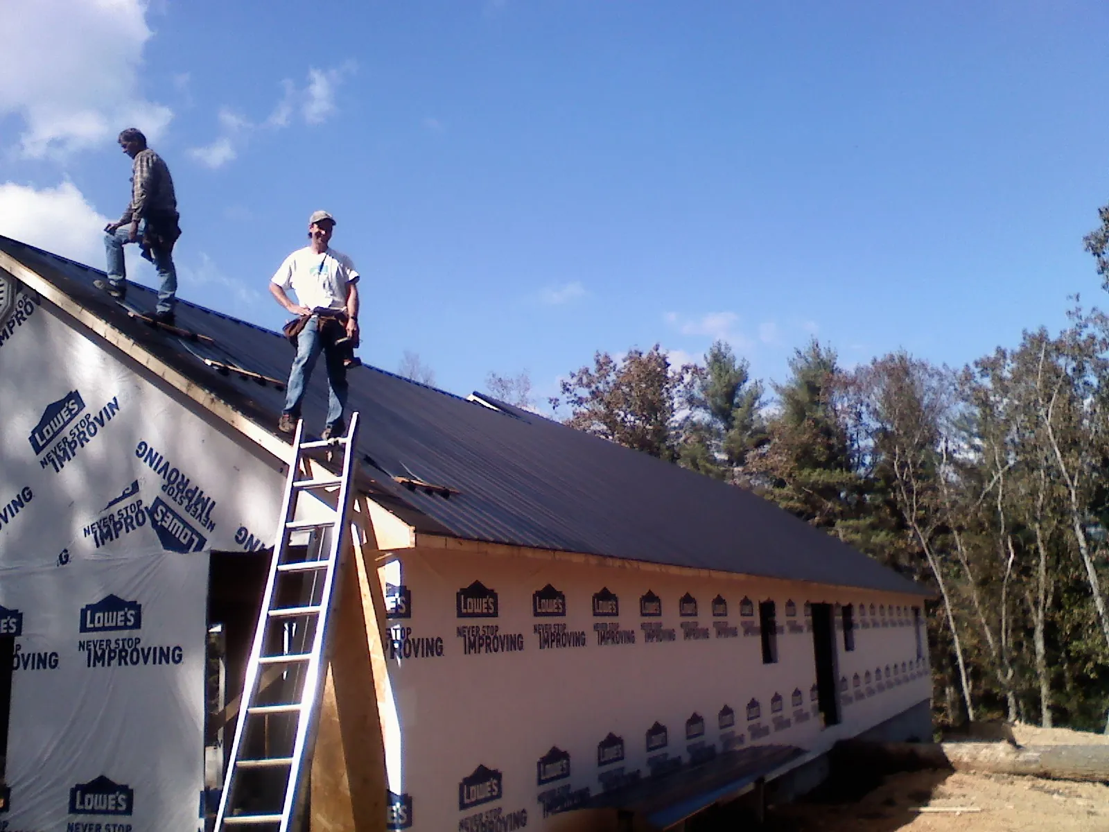 Two roofers standing on a long dark metal roof over a wrapped building in Southington